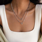 Close-up of a woman in a white square-neck top wearing the Paperclip Clasp Necklace—a layered silver chain featuring bold links, collectible charms, and circular pendants.