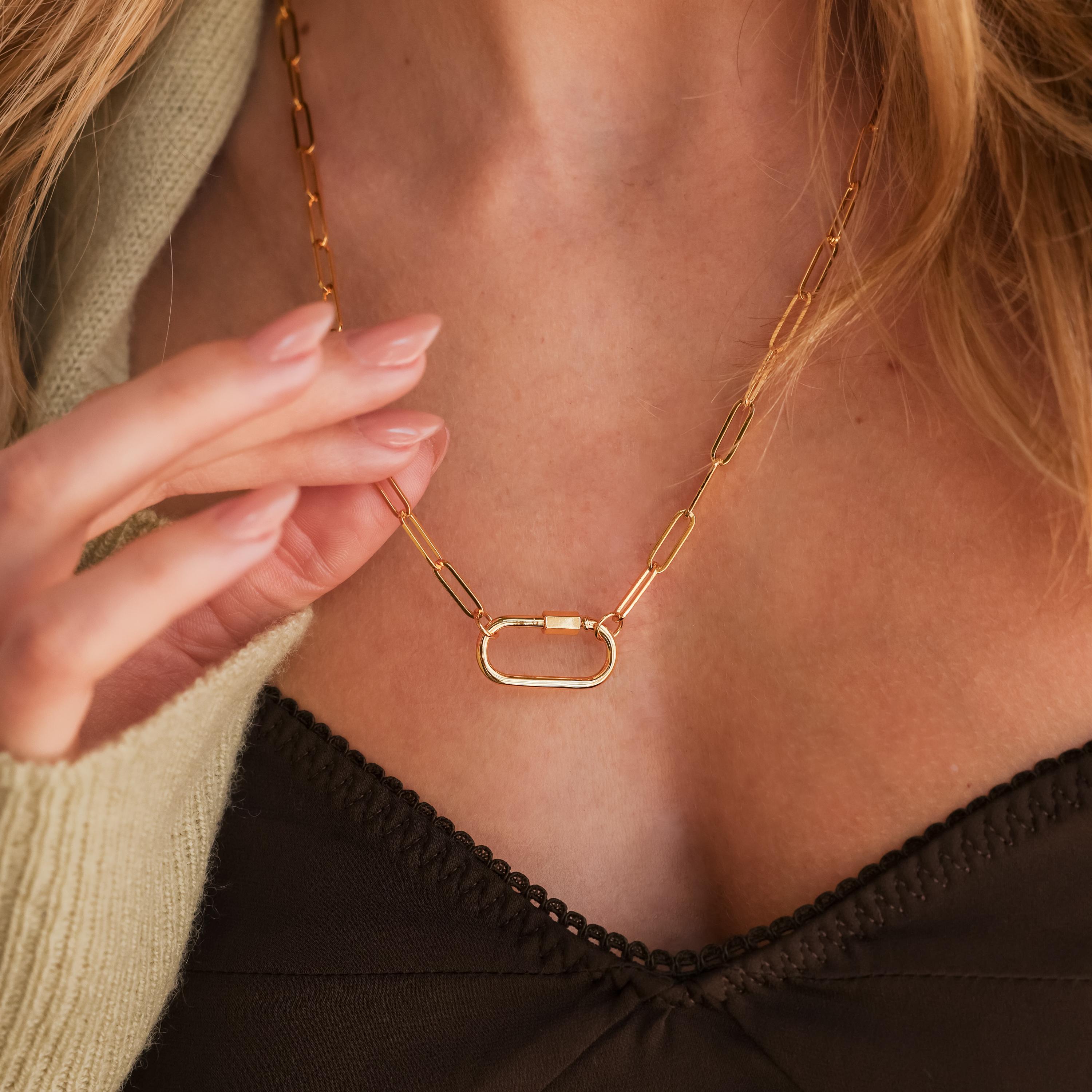 Close-up of a woman wearing the Bar & Carabiner Charm Set in 18K Gold, featuring an oval pendant and carabiner connector, touching it with her hand.