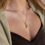 A woman wears the Multipurpose Charm Hoop Clasp Set in 18K Gold, styled with a letter A pendant and crystal charm, layered over a green cardigan and black top, creating a chic look with stacked bracelets.