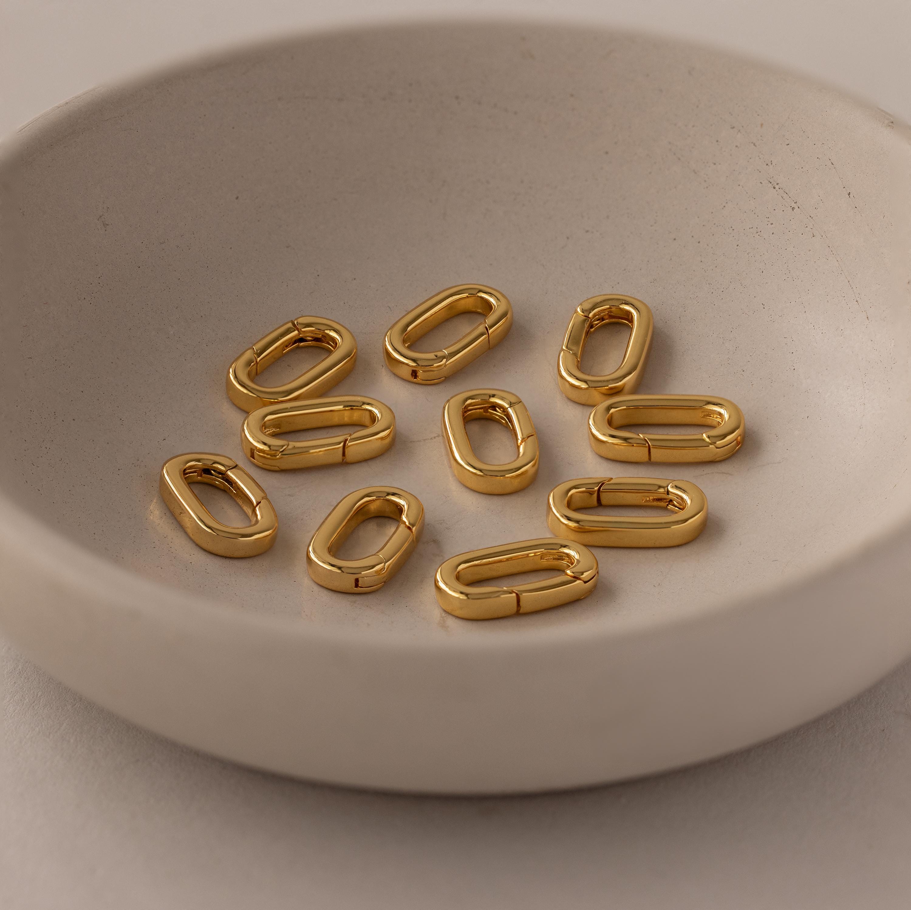 A ceramic bowl holds several shiny, oval Multipurpose Charm Hoop Clasp Sets in 18K Gold—ideal as versatile connectors for bracelet stacking—displayed on a neutral background.