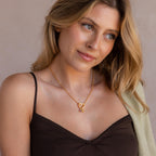 A blonde woman wears a brown camisole and drapes a light green sweater on one shoulder, accessorized with the Rolo Heart Clasp Necklace, which features a distinctive heart-shaped clasp for a touch of romance.