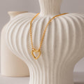 The Rolo Heart Clasp Necklace with a heart-shaped clasp is draped over a textured white ceramic vase, with another vase visible in the background.