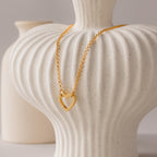 The Rolo Heart Clasp Necklace with a heart-shaped clasp is draped over a textured white ceramic vase, with another vase visible in the background.