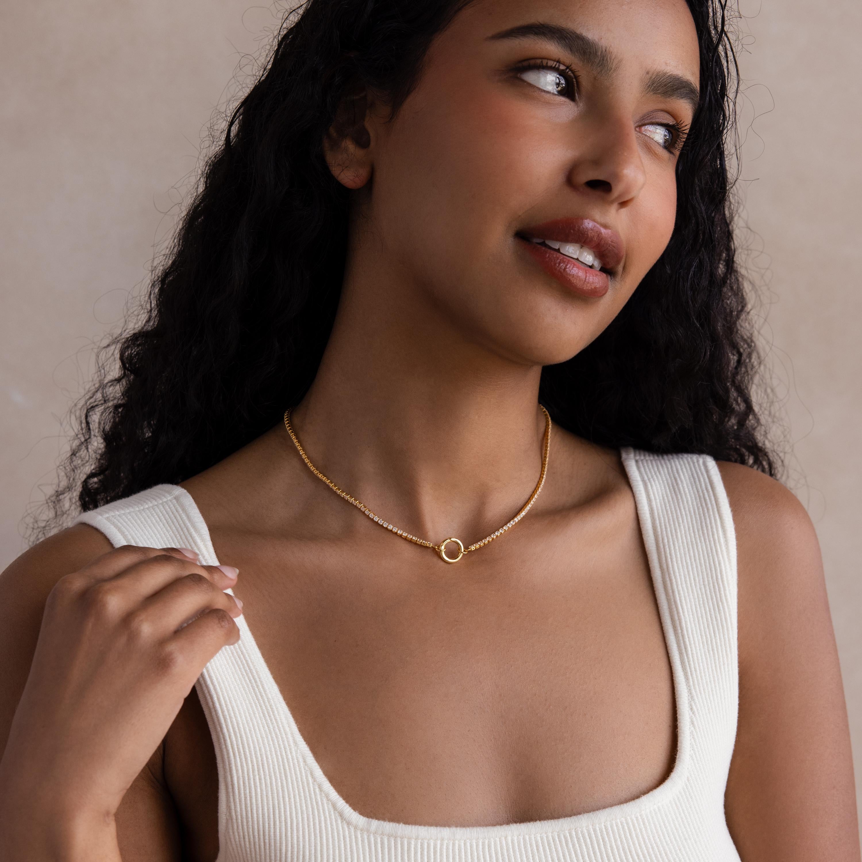 Woman with long curly hair wearing the Diamond Tennis Clasp Necklace in 18K Gold with a rolo clasp, paired with a white top, smiling and looking slightly to the side.