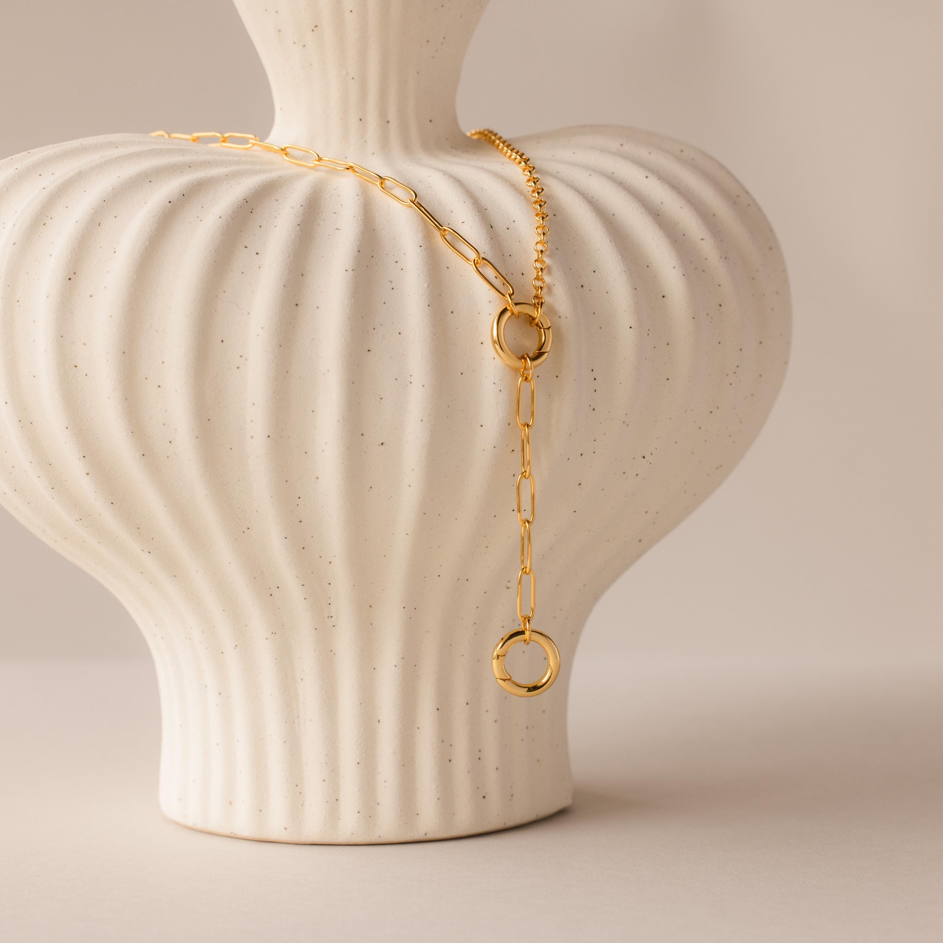 A Rolo Lariat Paperclip Clasp Necklace draped over a white textured ceramic vase with vertical grooves.