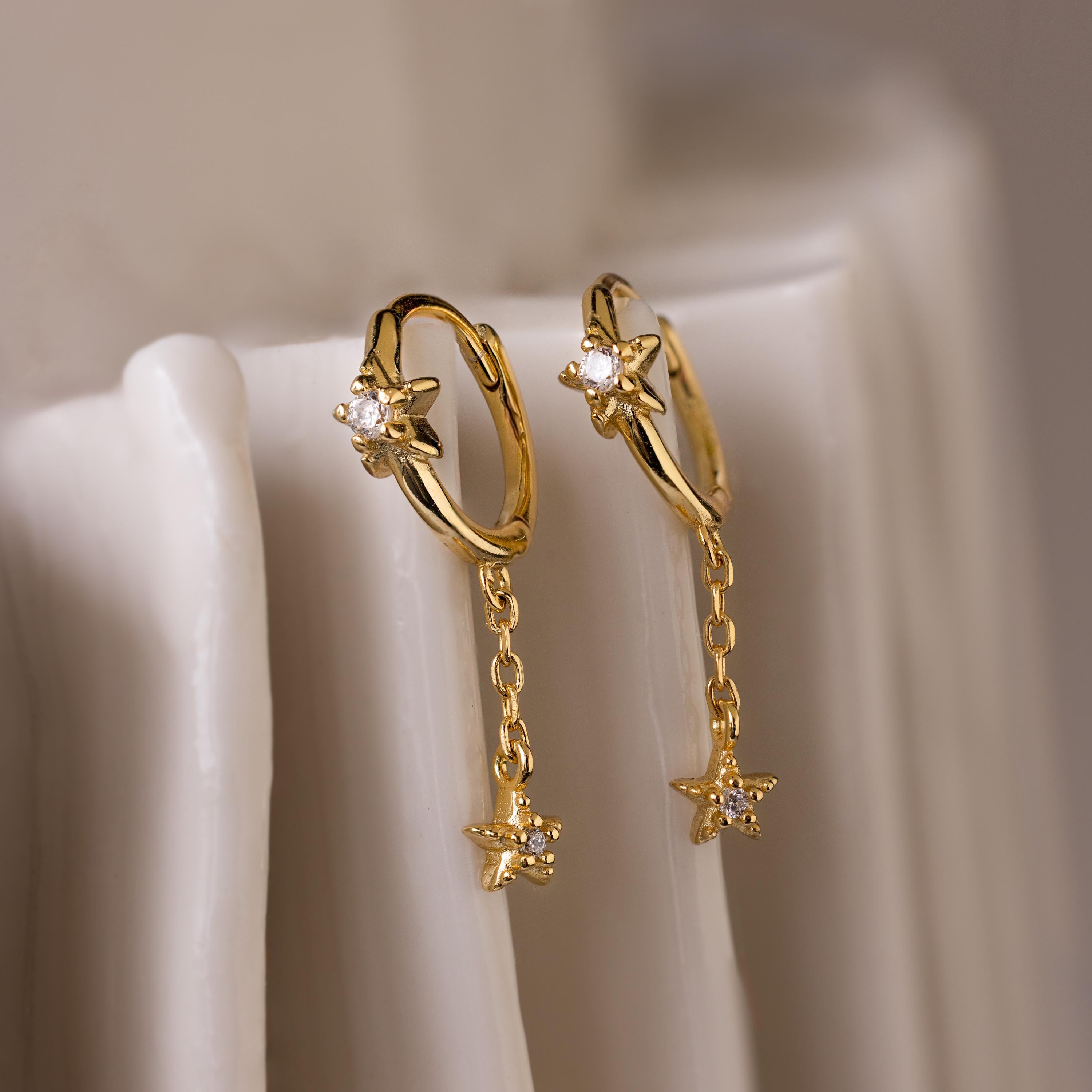 Close up of Gold Star Drop Chain Earrings floating on fabric