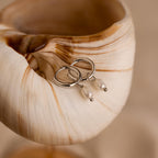 Close-up of Dainty Silver Pearl Huggies laying on a seashell