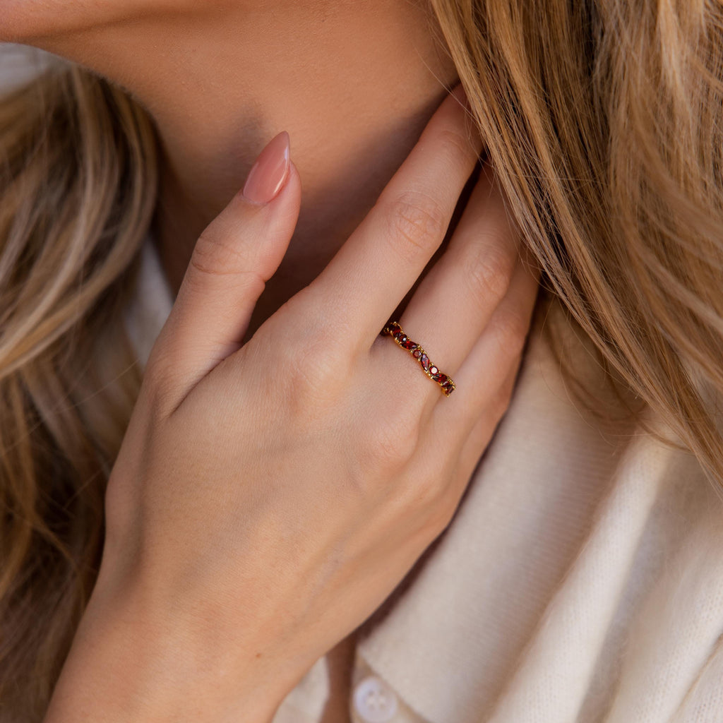 A woman touches her neck, displaying the Staggered Marquise Birthstone Ring with red gemstones on her finger.