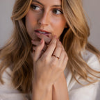 A blonde-haired woman gazes thoughtfully to the side, hands near her face, wearing the Staggered Marquise Peridot Ring.
