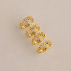 Four Multiple Name Eternity Rings in 18K Gold, each personalized with cut-out names, are arranged vertically on a beige textured surface—a unique gift to celebrate your loved ones.