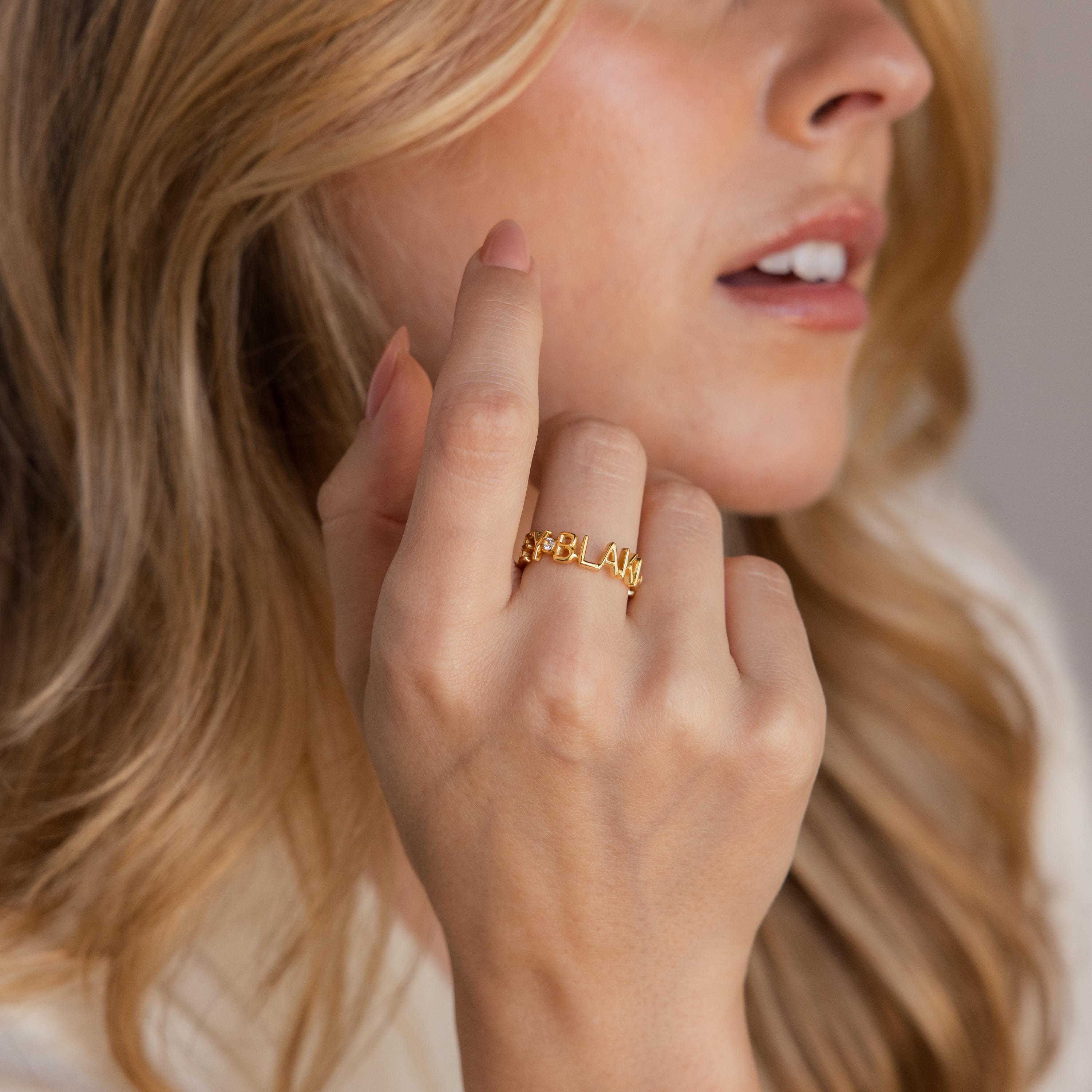 A woman with wavy blonde hair wears the Multiple Name Eternity Ring engraved with BLAKE, creating a meaningful gift for mom.