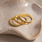 The Art Deco Emerald Eternity Ring, along with two other gold rings, rests on a speckled, wavy ceramic dish.