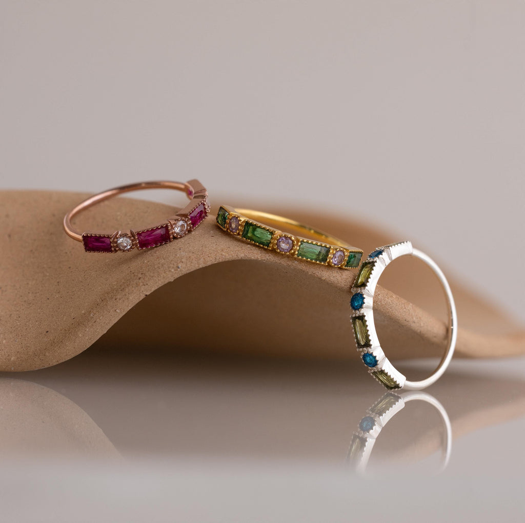 The Mixed Art Deco Birthstone Ring in Sterling Silver is displayed on a smooth, curved beige surface with a soft background.