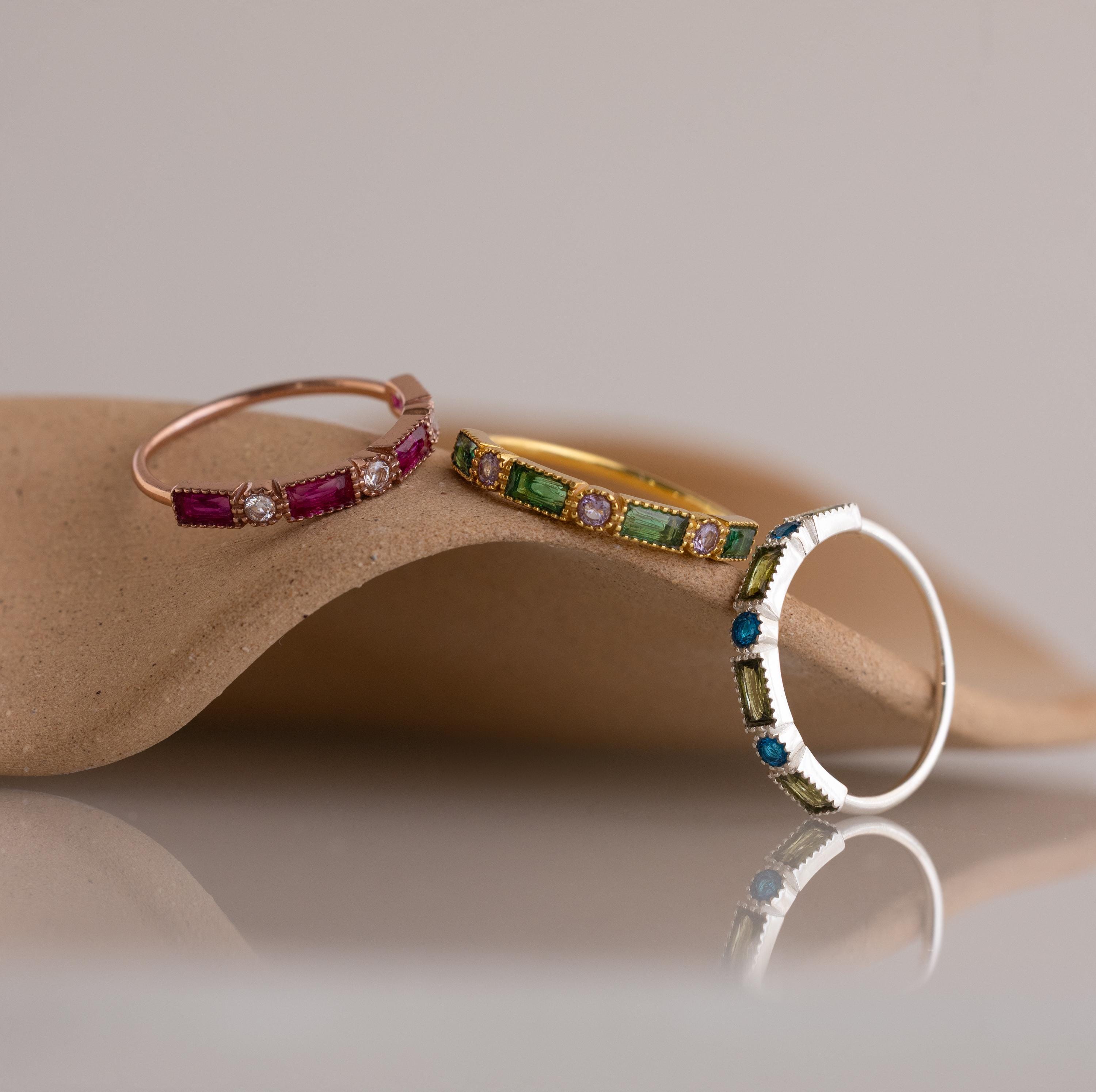 The Mixed Art Deco Birthstone Ring in Sterling Silver is displayed on a smooth, curved beige surface with a soft background.