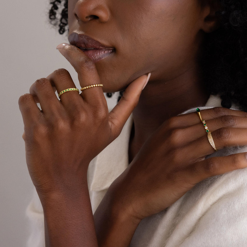 A woman with gold rings, including the Art Deco Onyx Eternity Ring, touches her face, showing off her manicured nails and vintage-inspired jewelry.