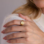 A woman’s hand wearing the Pave Initial Signet Ring rests on her shoulder, adding a touch of sparkle to her white sweater.