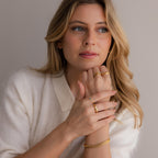 Woman with wavy blonde hair wears gold rings, including the Duo Initial Peridot Tennis Ring, and a bracelet, styled in a white collared sweater.