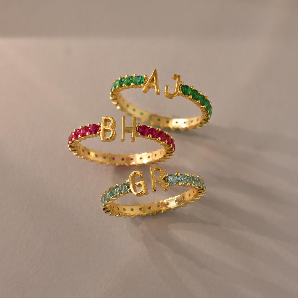 Three Duo Initial Onyx Tennis Rings, each with colored gemstones and initials AJ, BH, and GR, displayed on a light surface—a stunning personalized touch for every eternity band.