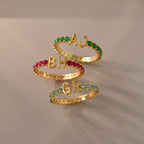 Three Duo Initial Onyx Tennis Rings, each with colored gemstones and initials AJ, BH, and GR, displayed on a light surface—a stunning personalized touch for every eternity band.