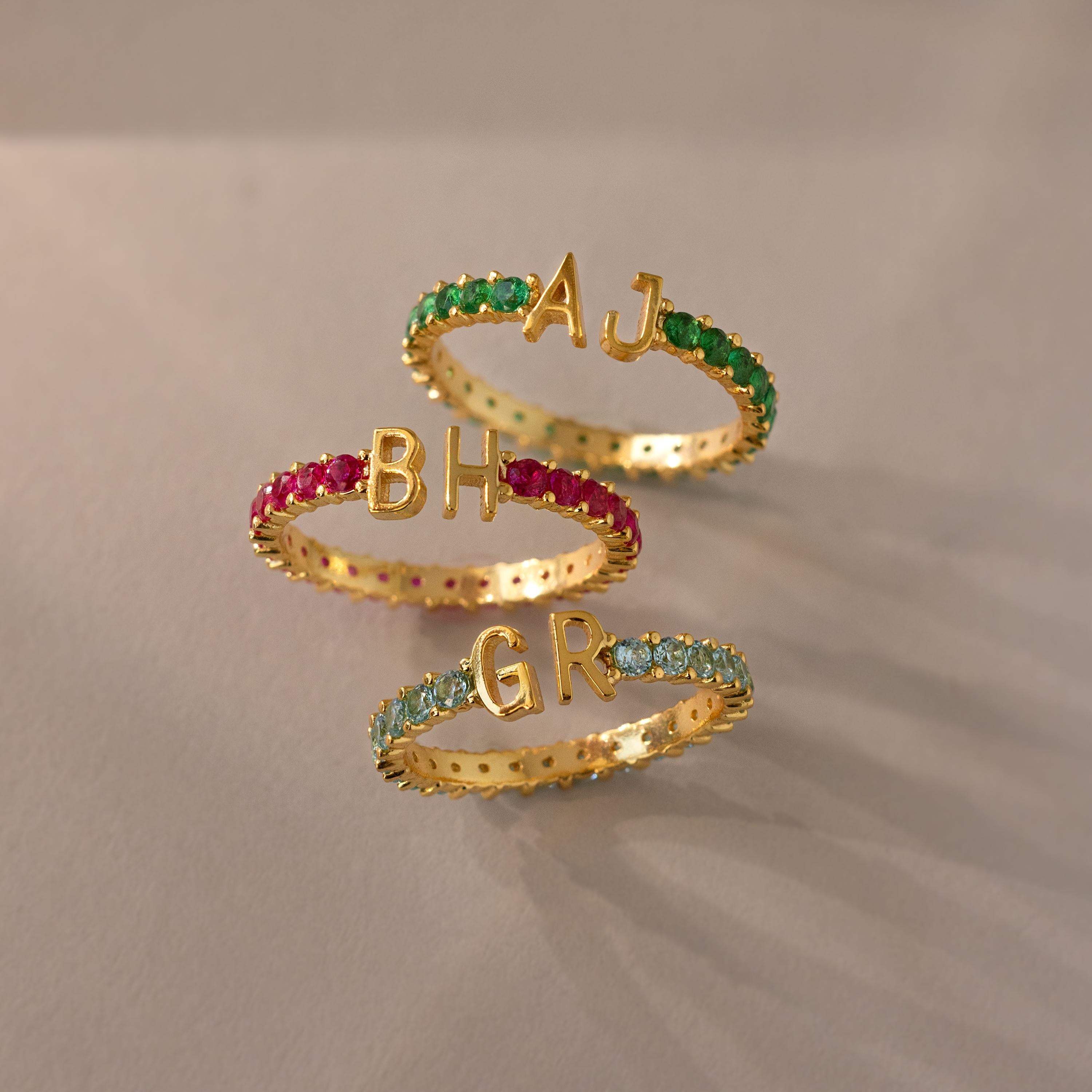 Three Duo Initial Onyx Tennis Rings, each with colored gemstones and initials AJ, BH, and GR, displayed on a light surface—a stunning personalized touch for every eternity band.