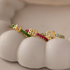 A Duo Initial Peridot Tennis Ring featuring two custom gold initials and sparkling peridot gems rests on a white, sculpted surface resembling teeth.