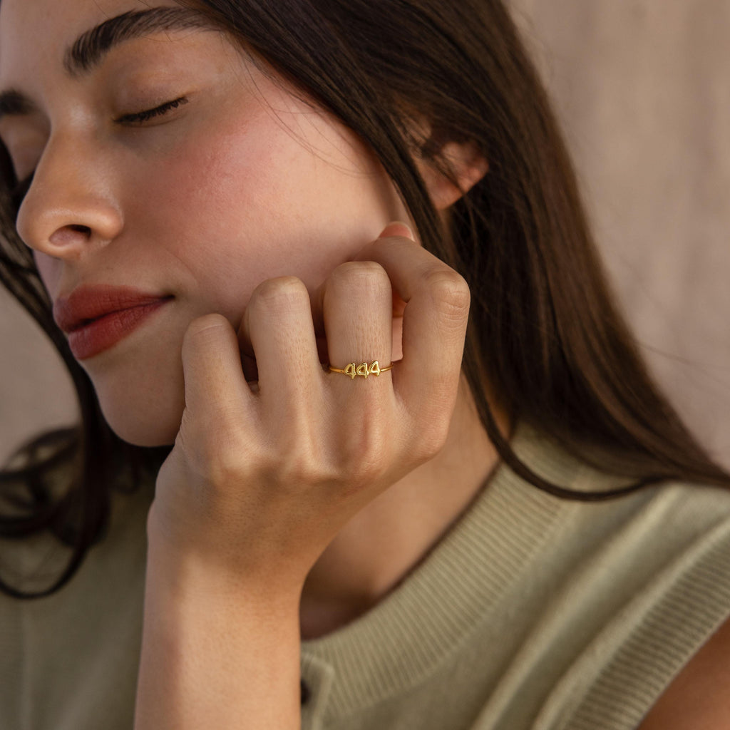 A model gently rests her face on her hand wearing a gold “1994” ring.