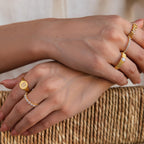 Two hands rest on a woven surface, each adorned with the sparkling Pave Initial Signet Ring in 18K Gold, beautifully showcasing the jewelry's diamond accents.