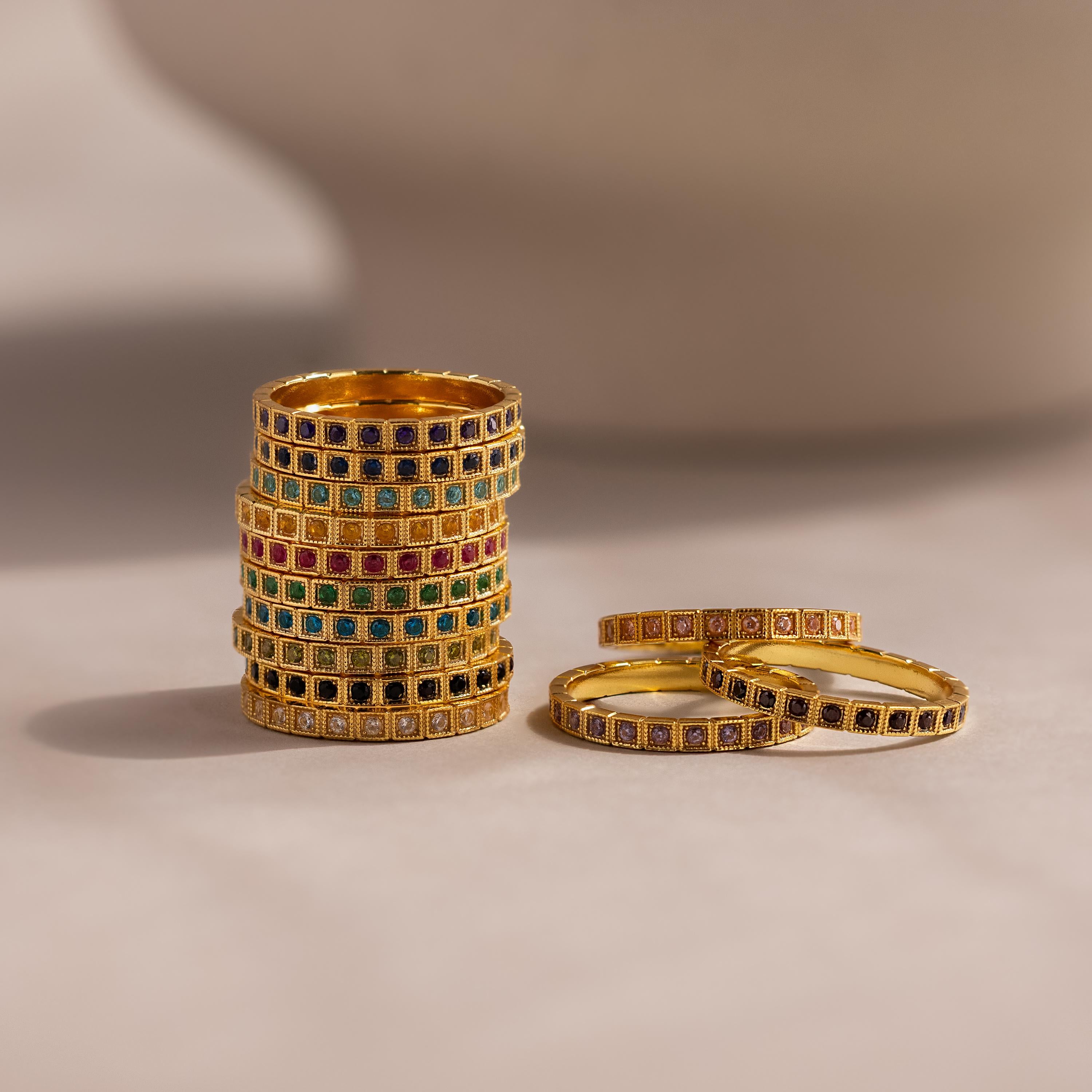 The Art Deco Onyx Eternity Ring features stacked gold bands with colorful square gemstones, evoking vintage-inspired jewelry on a neutral background.