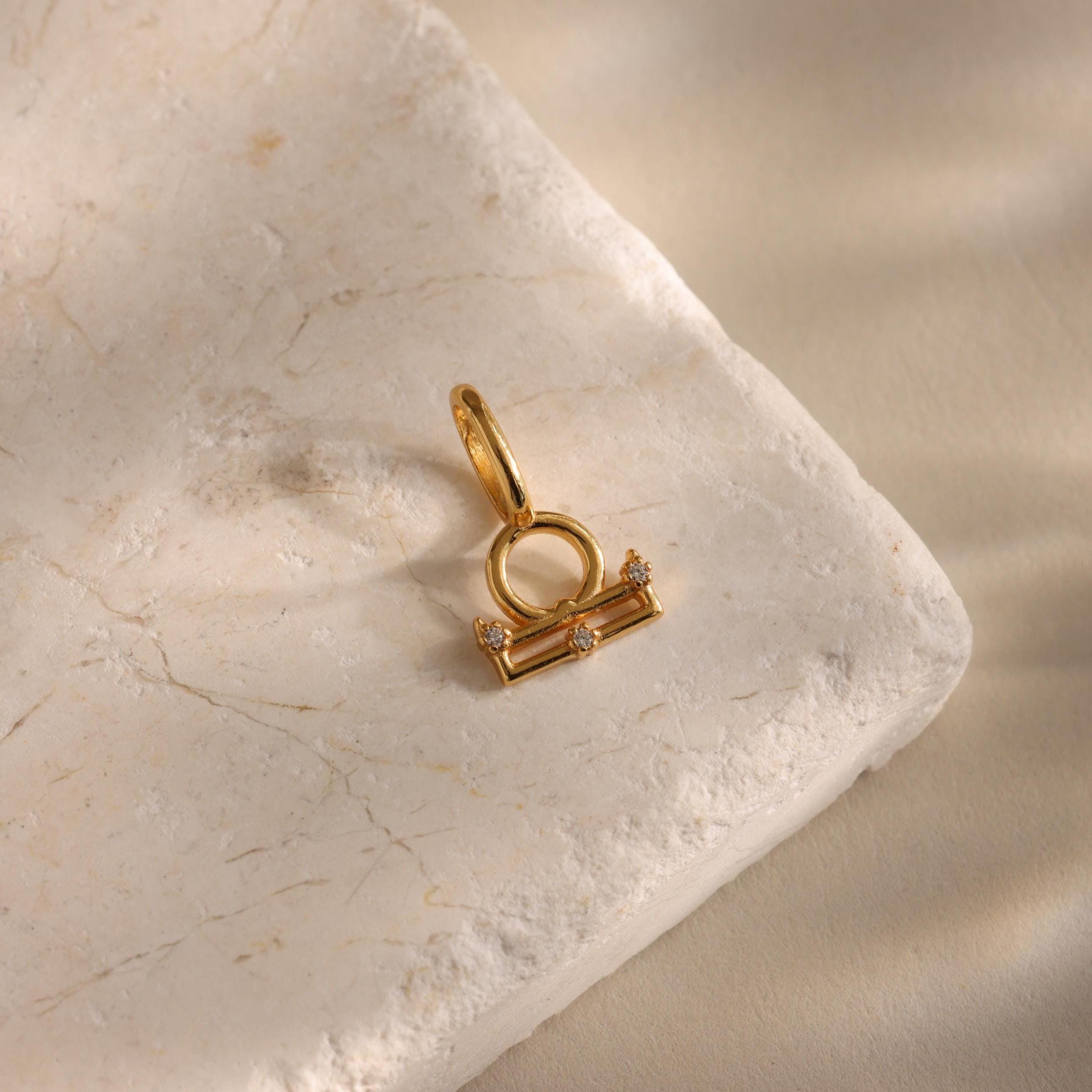A single Libra zodiac charm pendant rests on a stone background