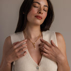 A model wears the North Star Hand Charm on a rolo clasp necklace centered on her chest, styled with a minimal cream knit top.