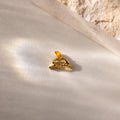 A single gold Heart Hands charm is styled on a soft neutral background near a light stone.