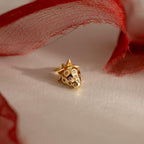 A close-up of a gold strawberry charm with crystal accents, lying on a flat surface partially wrapped in red tulle fabric.