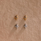 One pair of gold Pave North Star Earrings and one pair of silver Pave North Star Earrings displayed on a tan surface