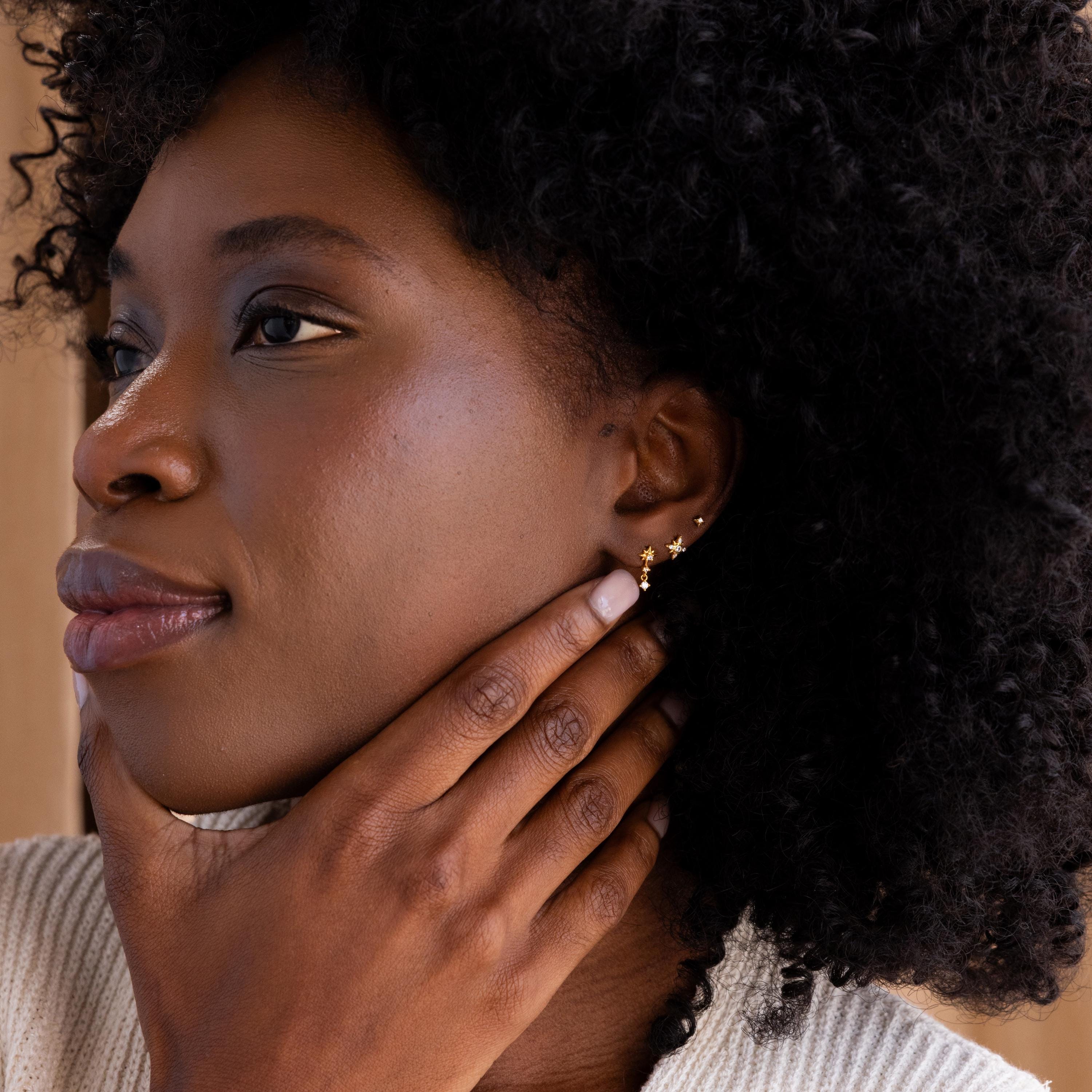 Far shot of Pave North Star Earrings on a model's ear in the center, with a smaller star earring and a larger star drop earring aside them