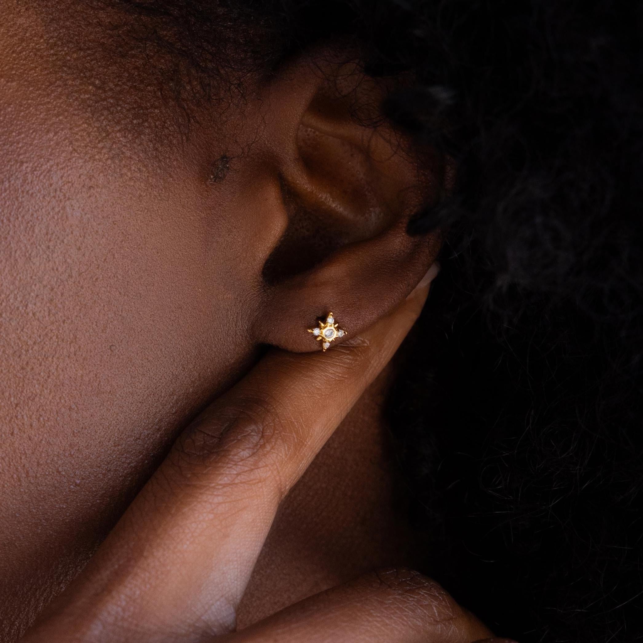 Close up of Pave Diamond North Star Earrings on model's ear. Earrings have a round diamond in the center and other diamond stones arranged in a star shape