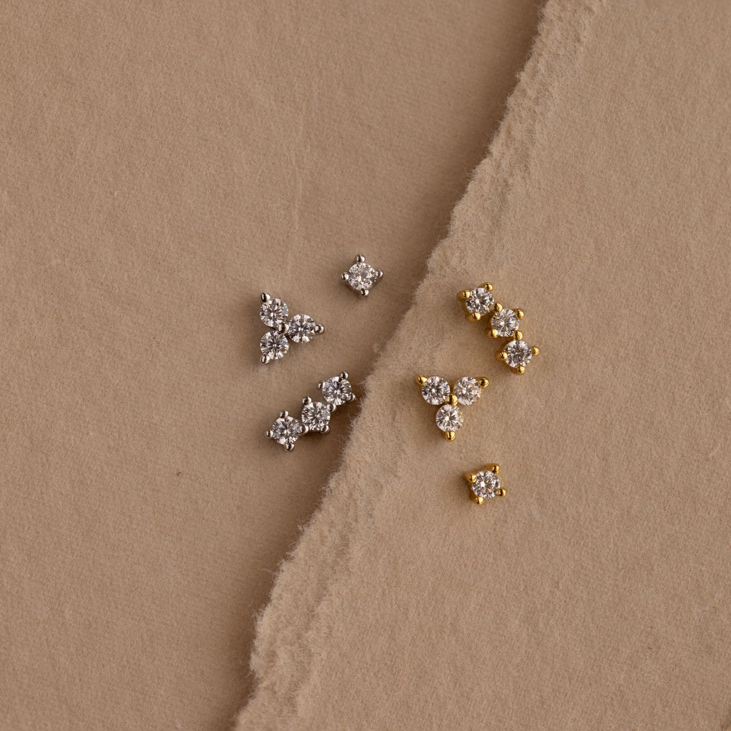 Set of 3 silver dainty CZ Diamond Constellation Studs next to set of 3 gold dainty CZ Diamond Constellation Studs displayed on a beige background