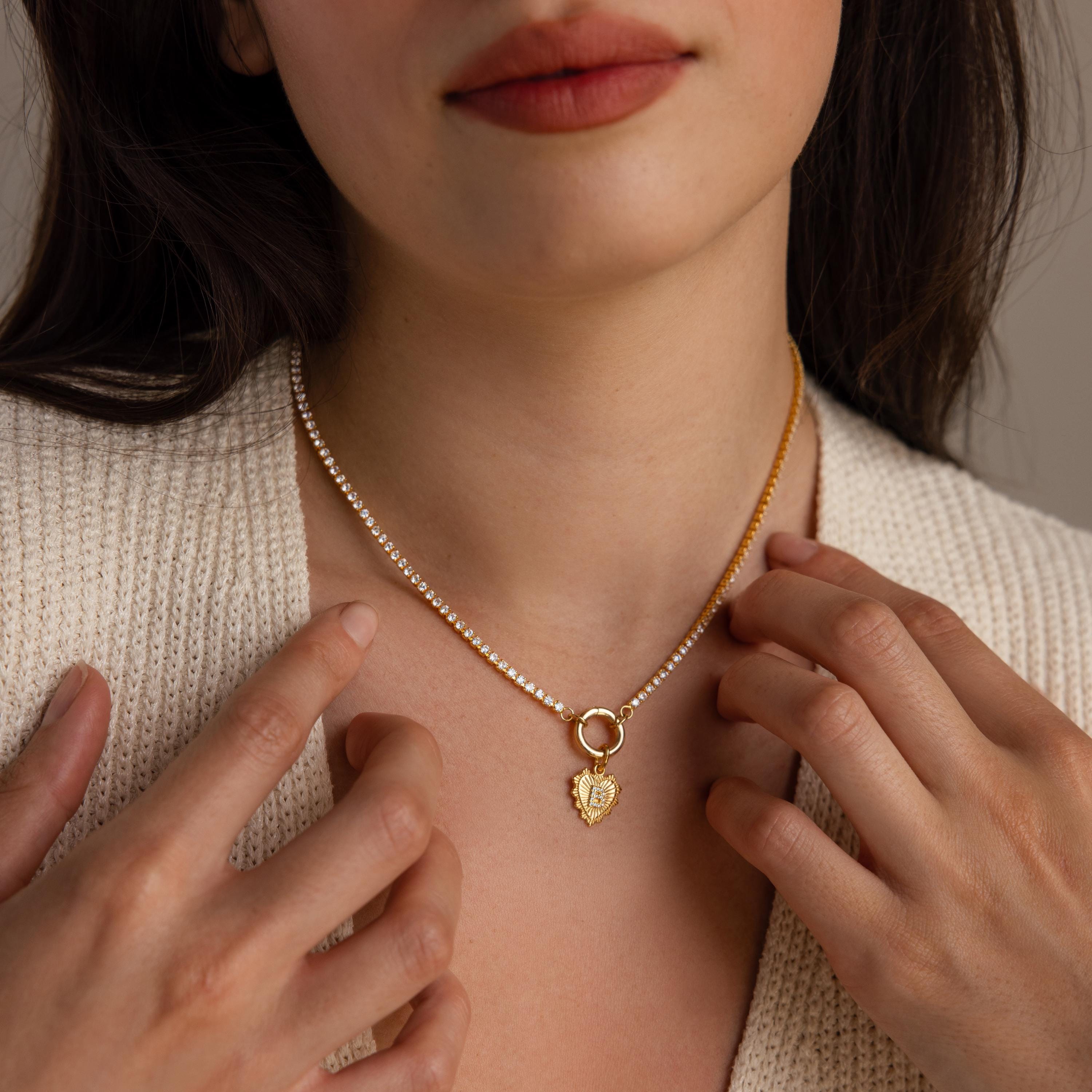 Model gently touching the Ribbed Heart Initial Pendant as it lays on a diamond tennis clasp chain