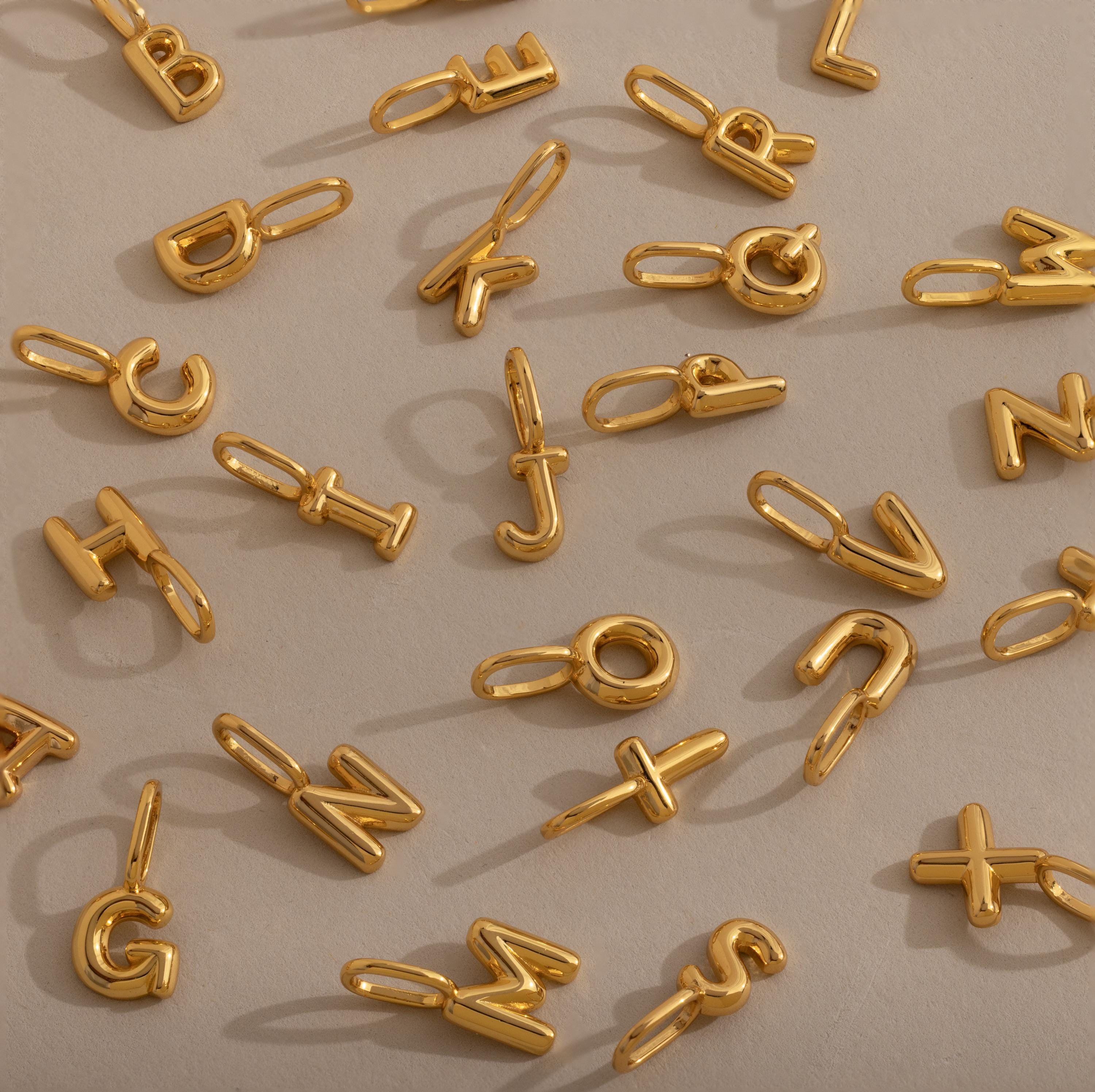 Bubble Letter Charms scattered on a beige surface—perfect for creating your own personalized jewelry collection.