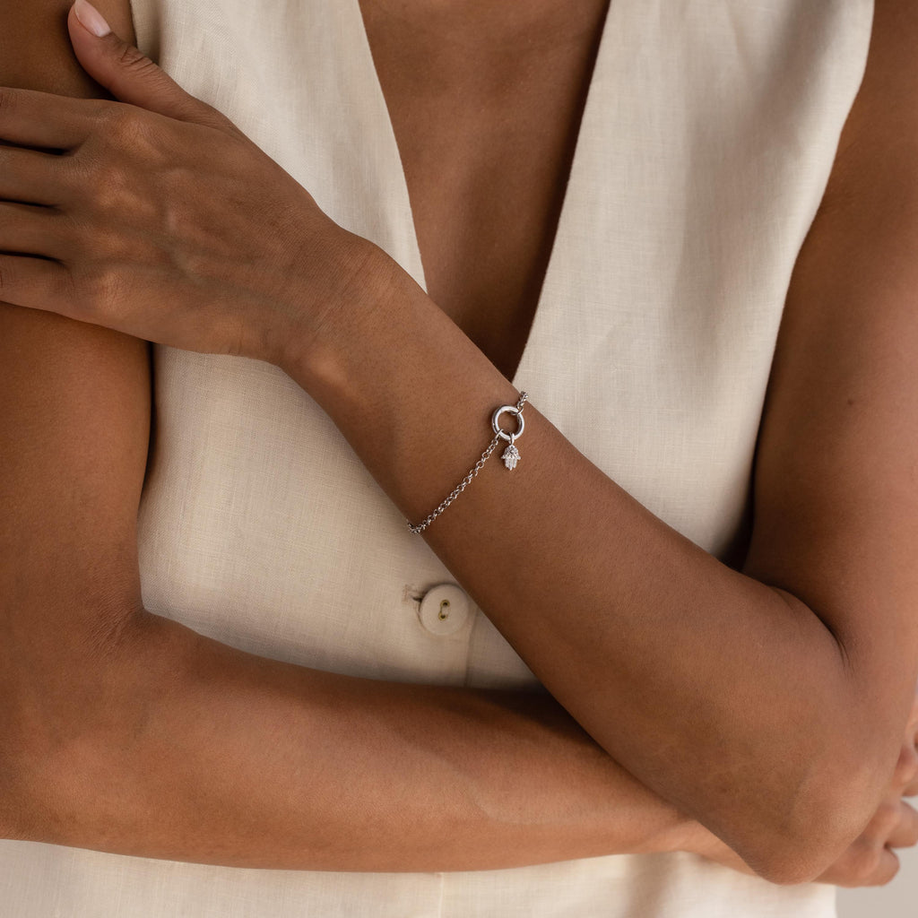 A full view of a model’s arm showing a silver Evil Eye Hand Charm bracelet worn with a light linen outfit.