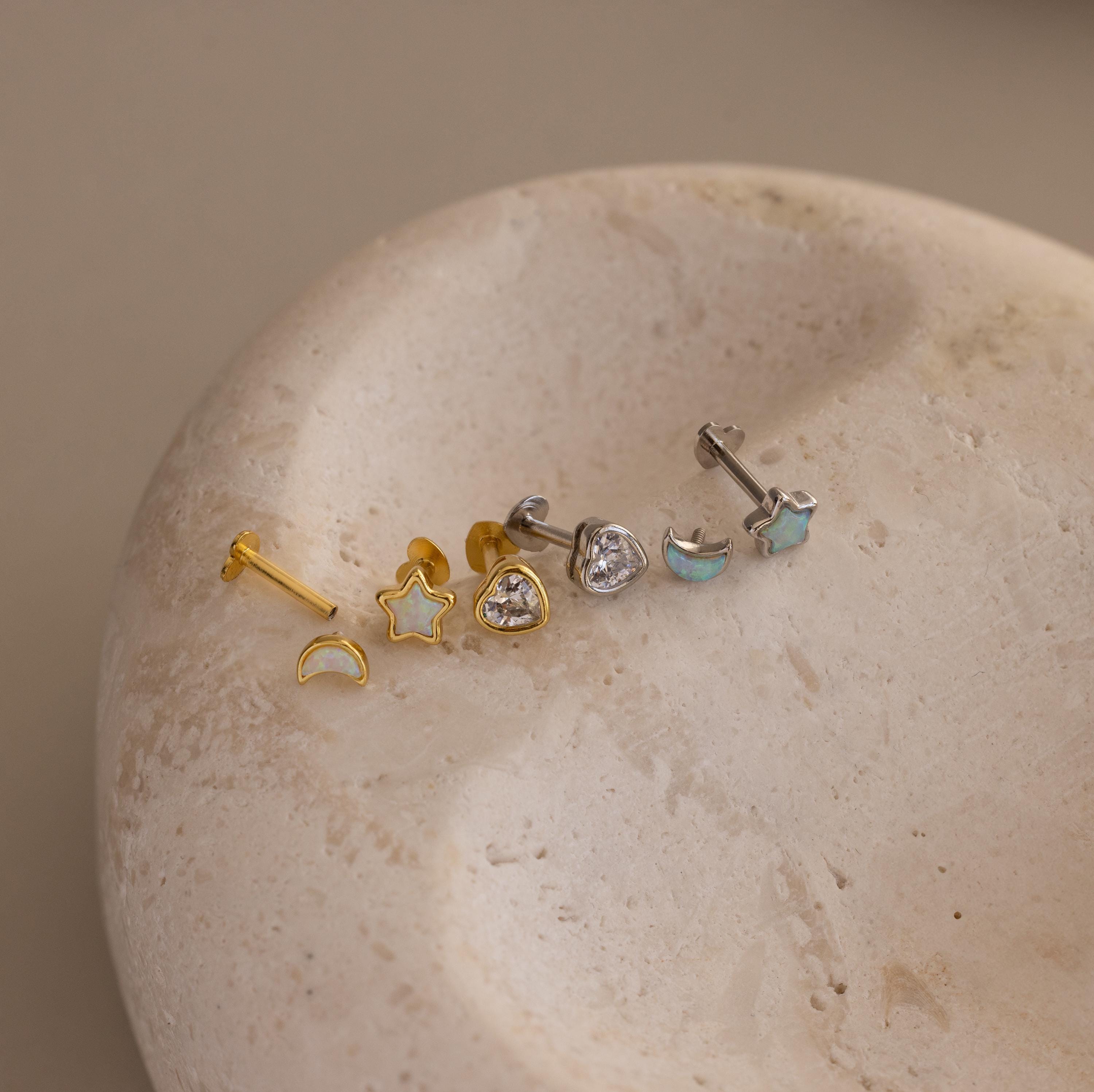 Flat lay of Gold & Silver Opal CZ Diamond Celestial Stud Earring Set with heart shaped flat backing unscrewed, displayed on round stone surface.