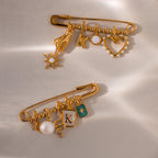 Two fully styled beaded safety pin charms laid flat—one features a celestial hand, opal star, initial K, and heart charm, while the other includes a pearl, snake, and green enamel charm.