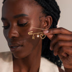 Woman holding a gold beaded safety pin charm in her hand, styled with a pearl, heart, and “k” charm.
