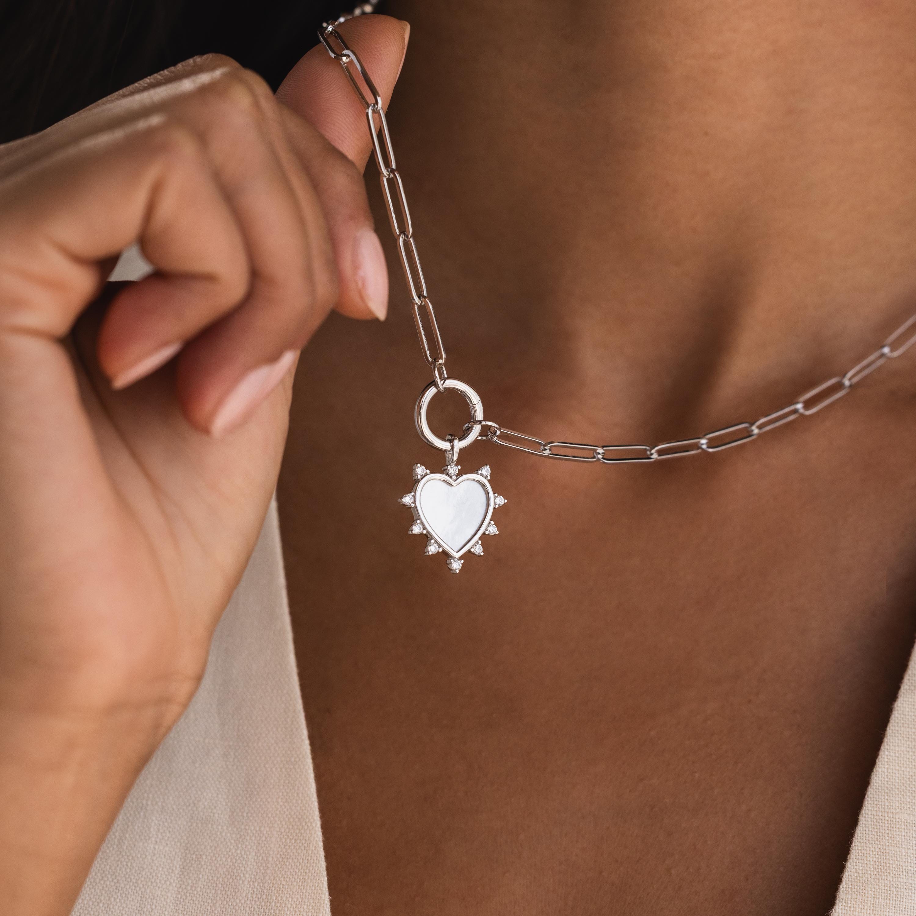 The silver Starburst Pearl Heart Charm is attached to a paperclip-style chain necklace and held up near the neck.