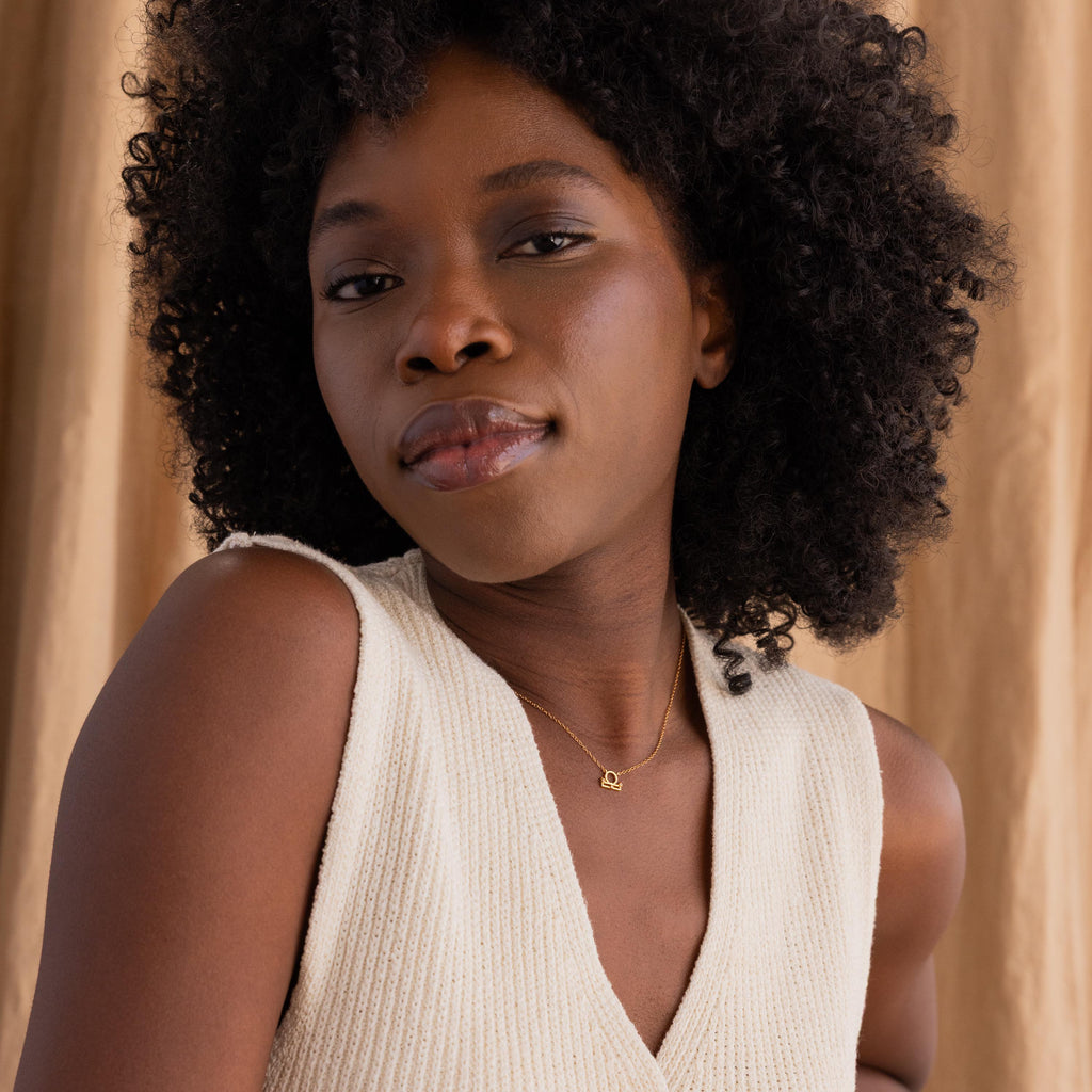 Wide shot of gold CZ diamond Libra Zodiac Charm Necklace hanging from model's neck.