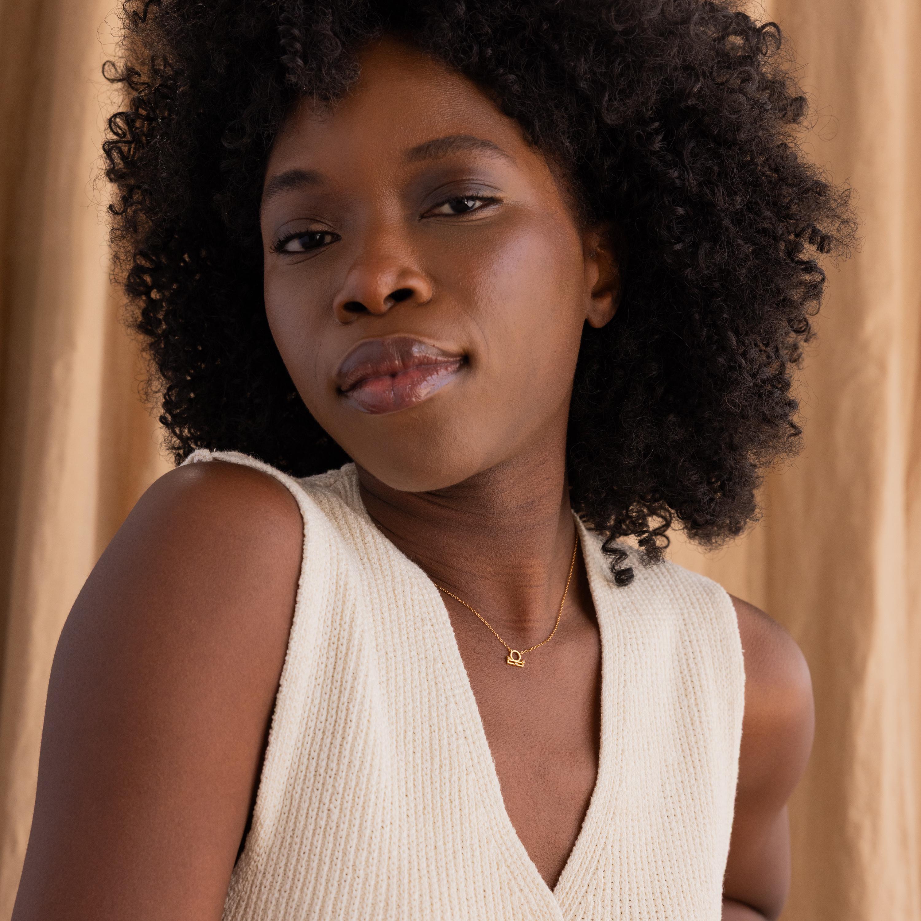 Wide shot of gold CZ diamond Libra Zodiac Charm Necklace hanging from model's neck.