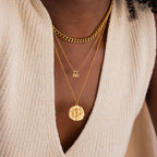 Model wears a gold CZ diamond libra zodiac charm necklace, layered with a thick gold curb chain on top and a hammered libra zodiac circle coin pendant on bottom.