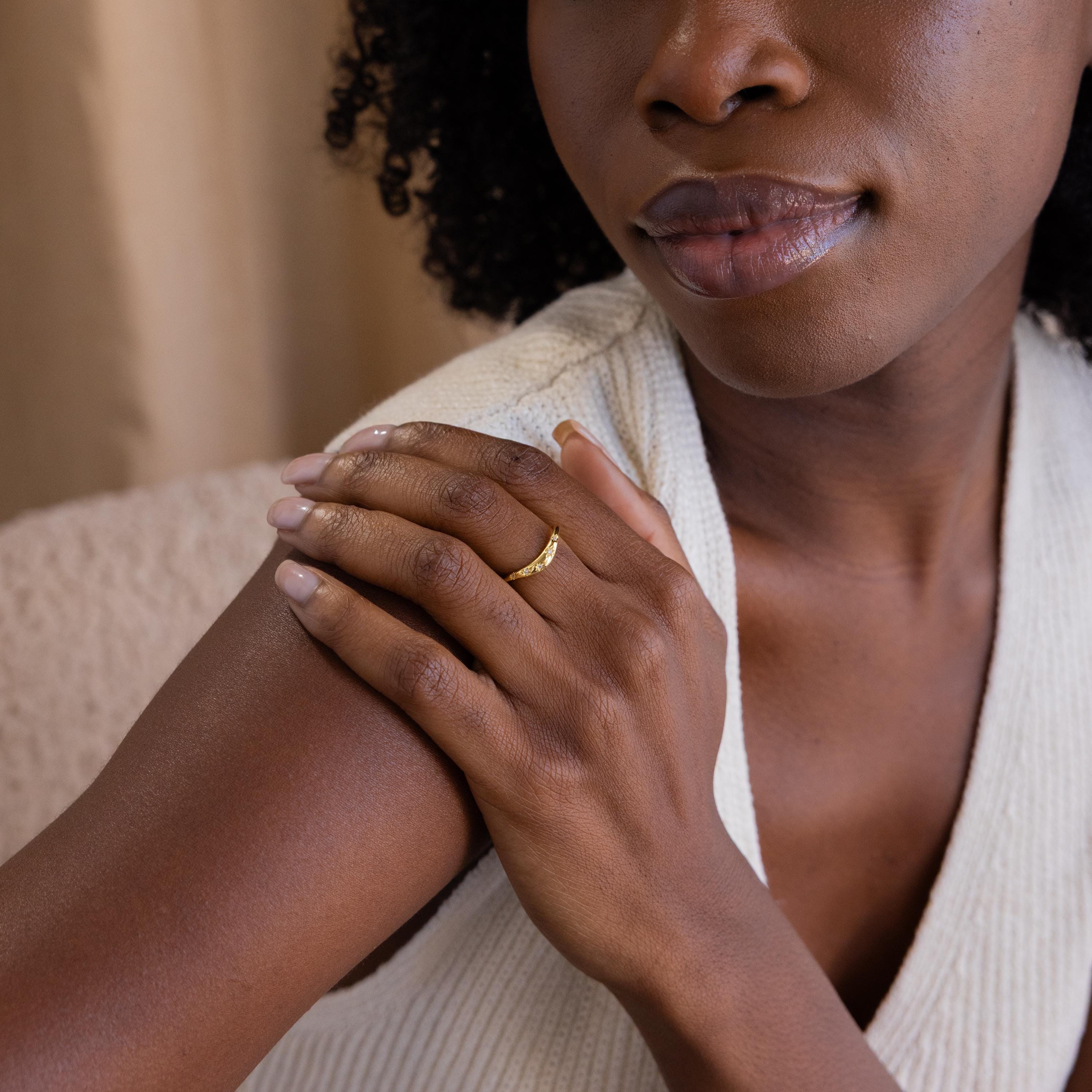 Celestial Wave Ring on model's middle finger. The gold ring features diamonds embedded within a star shaped design dotted sporadically on the face of the curved ring.