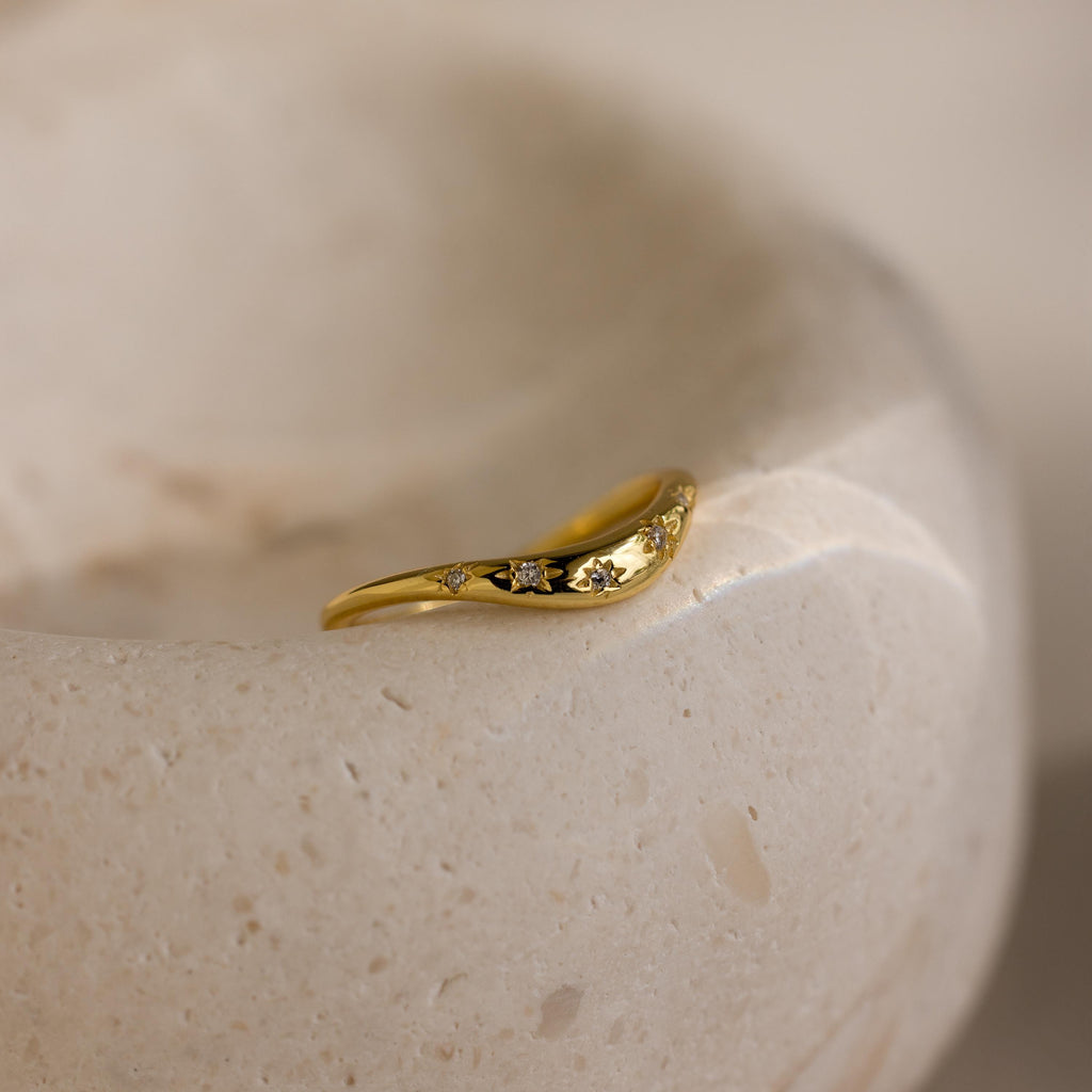 Close up of a gold celestial wave ring laying on a ceramic dish