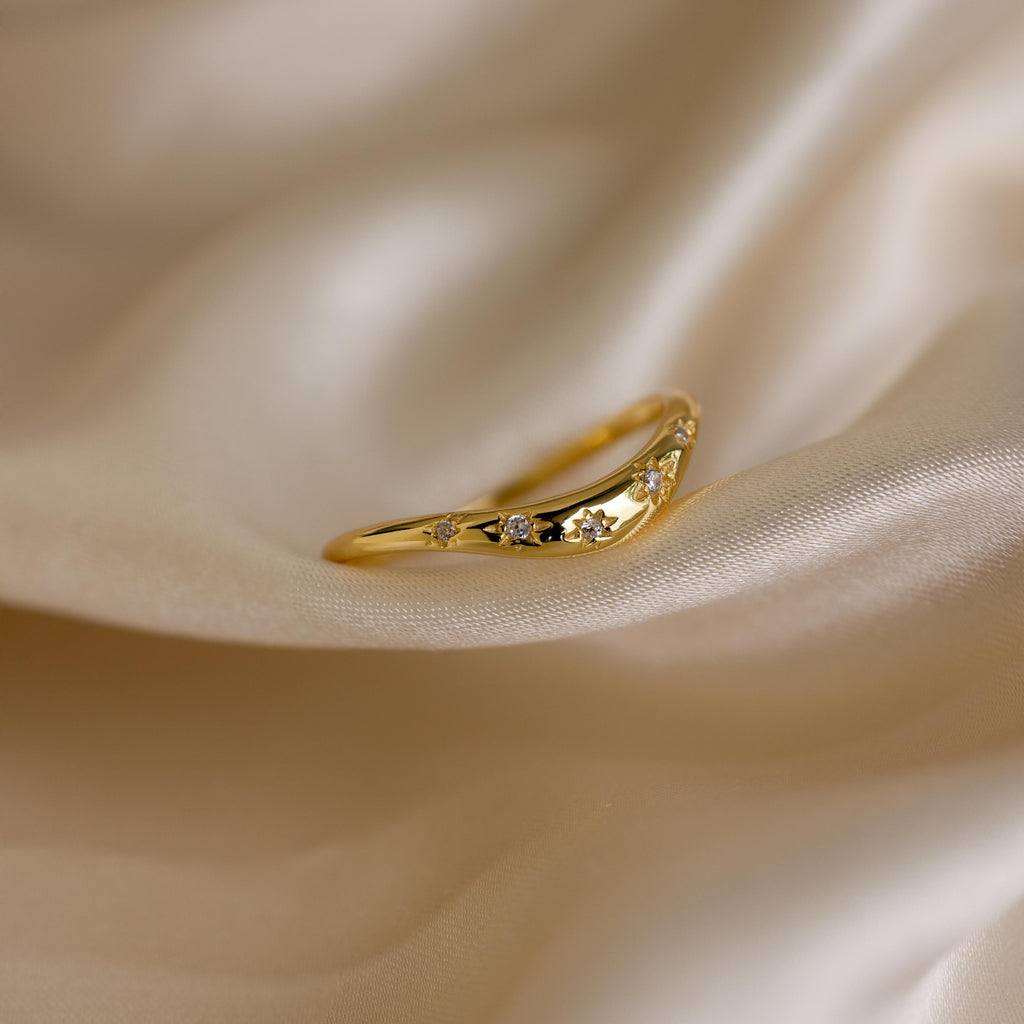 Close up of a gold celestial wave ring laying on a cloth surface