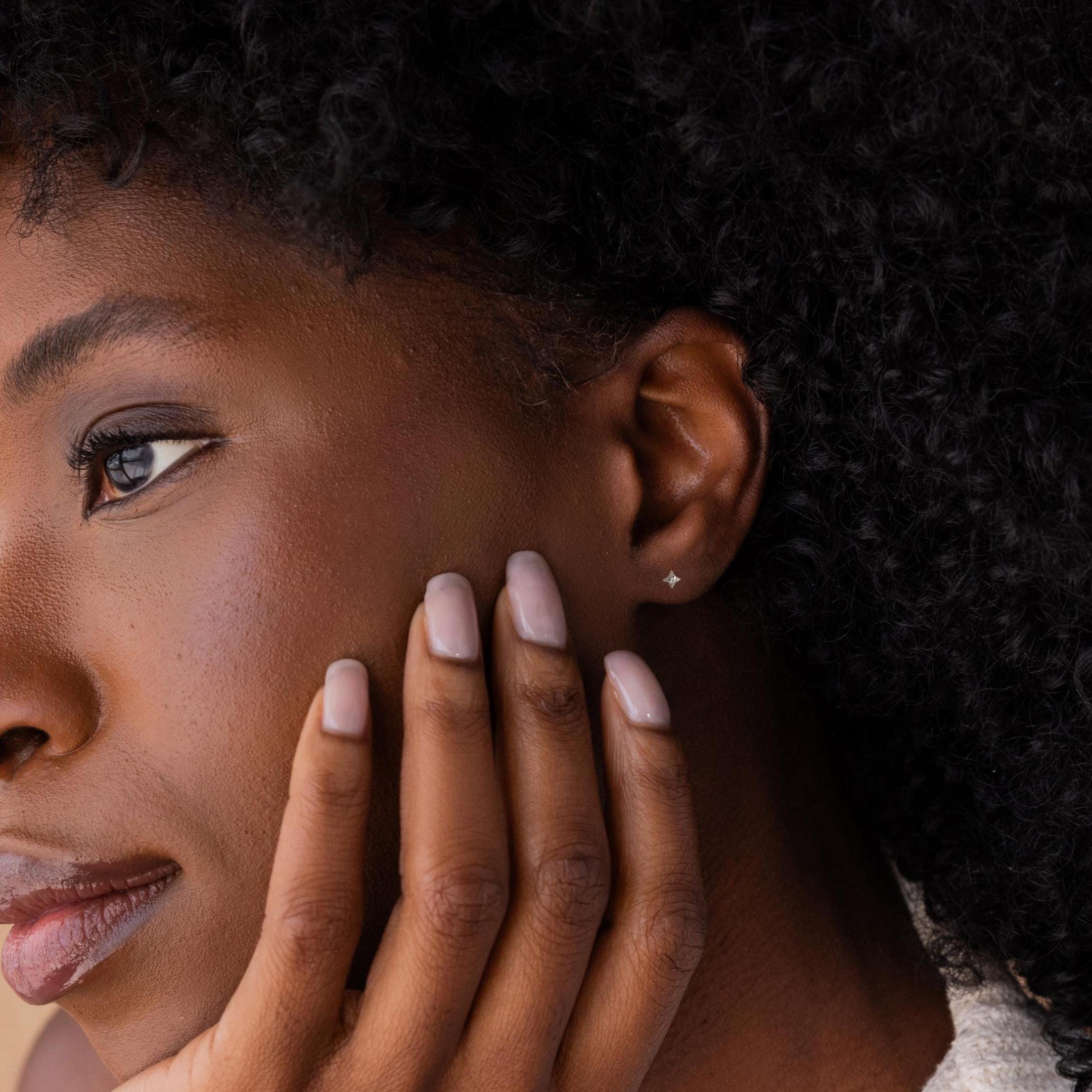 Close-up of a woman with natural curly hair touching her face, wearing North Star Flatback Studs in Sterling Silver that add a touch of celestial elegance.